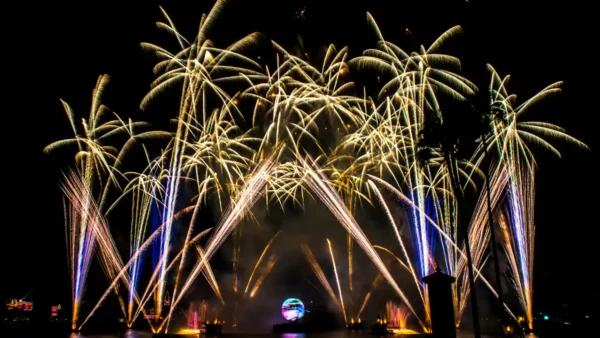 Un affichage d'illuminations vibrantes présentant des stries de lumière dorée s'arquant dans le ciel nocturne, rétro-éclairées par un orbe lumineux au centre, avec de faibles silhouettes de bâtiments en arrière-plan.