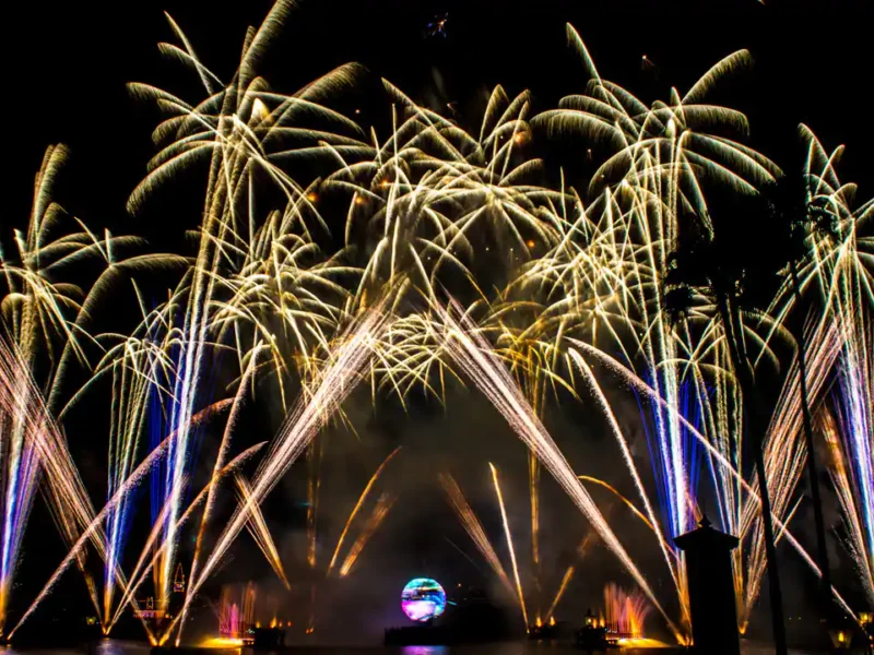 Un affichage d'illuminations vibrantes présentant des stries de lumière dorée s'arquant dans le ciel nocturne, rétro-éclairées par un orbe lumineux au centre, avec de faibles silhouettes de bâtiments en arrière-plan.