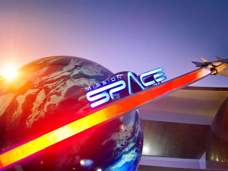 Une image vibrante de l'attraction « Mission Space » à Epcot, Disney World, présentant un grand globe et un modèle de vaisseau spatial avec des lumières rouges et bleues illuminées sous un ciel crépusculaire.