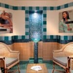 Une salle de relaxation spa à l'hôtel Disneyland avec deux chaises en osier faisant face à une pièce d'eau centrale en mosaïque, entourée de murs carrelés et ornée d'affiches de soins spa.
