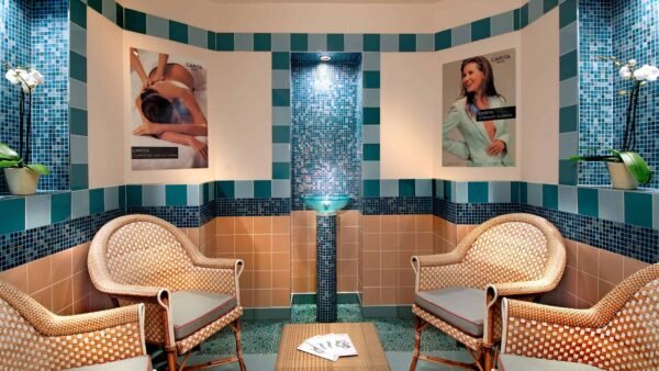 Une salle de relaxation spa à l'hôtel Disneyland avec deux chaises en osier faisant face à une pièce d'eau centrale en mosaïque, entourée de murs carrelés et ornée d'affiches de soins spa.
