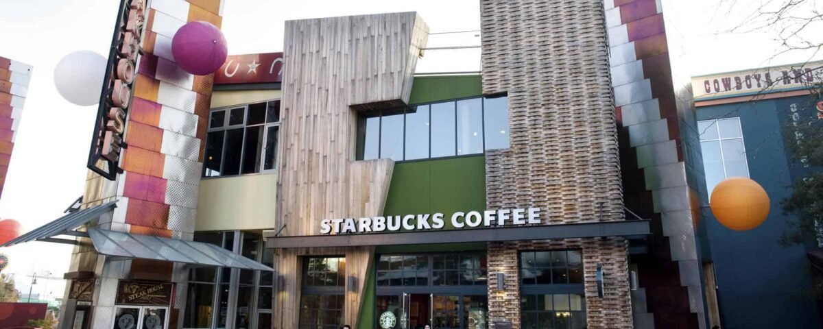 Vue extérieure d'un café Starbucks unique au design architectural moderne et éclectique, avec des carreaux colorés et un mélange de boiseries, avec des gens marchant devant.