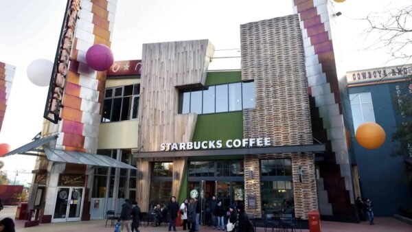 Vue extérieure d'un café Starbucks unique au design architectural moderne et éclectique, avec des carreaux colorés et un mélange de boiseries, avec des gens marchant devant.