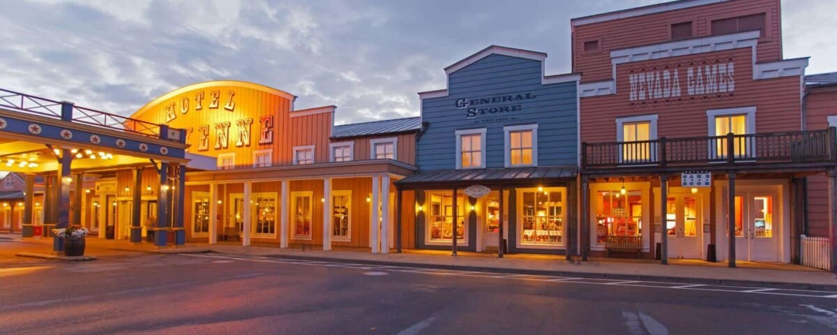 Une vue pittoresque d'une vieille ville pittoresque de l'Ouest au crépuscule, rappelant Disneyland Paris, avec des vitrines bien éclairées comprenant un hôtel, un magasin général et d'autres magasins sous un ciel spectaculaire.