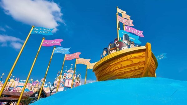 Une scène vibrante et colorée d'un manège dans un parc à thème, inspirée de « Le monde est petit », mettant en vedette un bateau pirate avec des personnages de dessins animés à bord, naviguant sur un ciel bleu vif avec une signalisation fantaisiste et