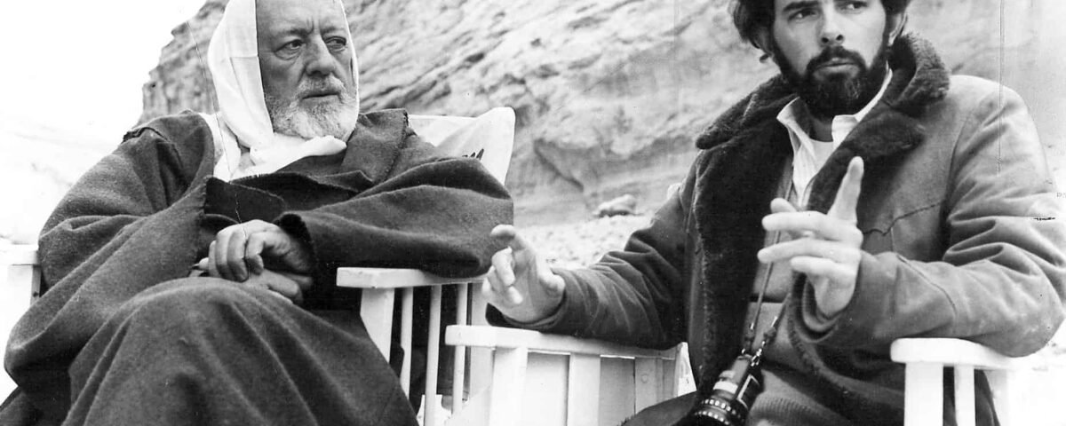 Deux hommes assis dehors, un plus âgé avec des cheveux blancs et une barbe ressemblant à George Lucas et un plus jeune avec des cheveux et une barbe bouclés, tous deux portant de gros manteaux, ont engagé une conversation sérieuse.