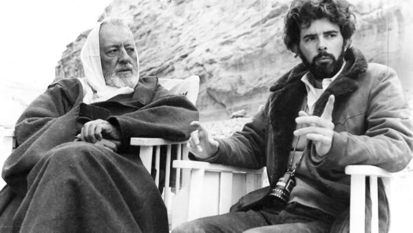 Deux hommes assis dehors, un plus âgé avec des cheveux blancs et une barbe ressemblant à George Lucas et un plus jeune avec des cheveux et une barbe bouclés, tous deux portant de gros manteaux, ont engagé une conversation sérieuse.