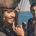 Un pirate des "Pirates des Caraïbes" avec un tricorne et des dreadlocks regarde pensivement sur le côté, tenant un petit télescope. A côté de lui se tient un jeune homme dans un