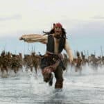 Le capitaine Jack Sparrow courant sur l'eau, poursuivi par une tribu, dans une scène dynamique et urgente de "Pirates des Caraïbes".