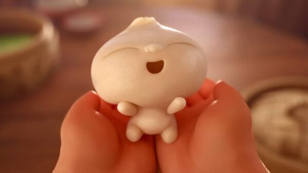 Un personnage de raviolis ravissants de style dessin animé avec bras et jambes, conçu à la manière de Disney en 2018, est tenu dans des mains humaines sur un fond de cuisine légèrement flou. La boulette a un
