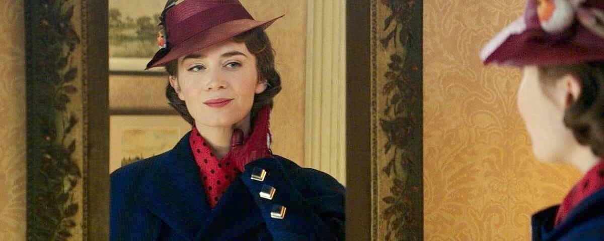 Une femme portant un chapeau marron vintage et un manteau bleu orné d'un foulard rouge regarde son reflet dans un miroir orné, ajustant son foulard avec une expression ravie rappelant "Mary Poppins Returns".