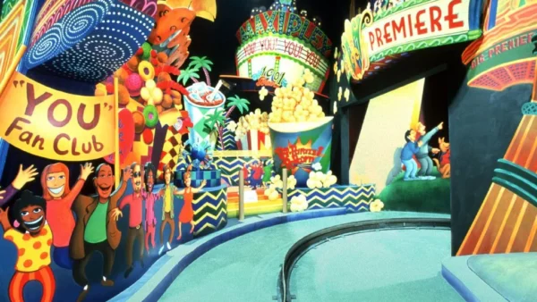 Parc à thème animé avec des personnages colorés et animés, dont une foule joyeuse et un clown, près du panneau « limousine superstar », sous une bannière « première ».