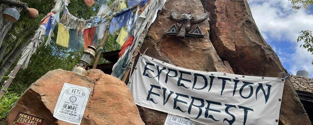 Un affichage d'entrée pour l'expédition Everest avec des bannières et un décor de sommet de montagne accidenté sous un ciel bleu avec des nuages épars.