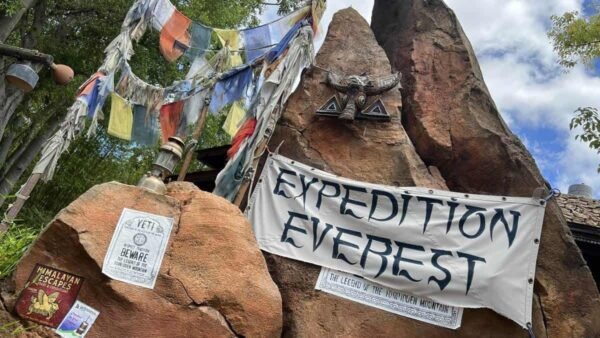 Un affichage d'entrée pour l'expédition Everest avec des bannières et un décor de sommet de montagne accidenté sous un ciel bleu avec des nuages épars.