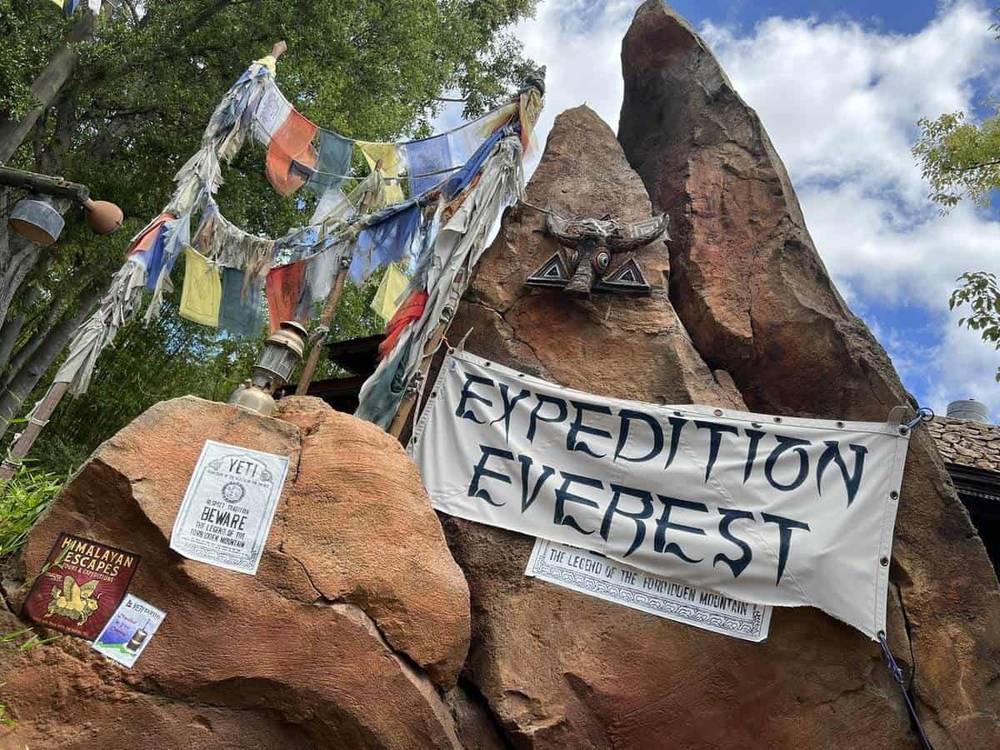 Un affichage d'entrée pour l'expédition Everest avec des bannières et un décor de sommet de montagne accidenté sous un ciel bleu avec des nuages épars.