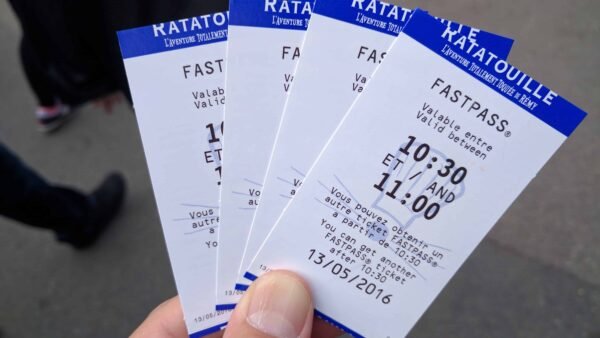 Une main tenant trois billets fastpass pour l'attraction Indiana Jones et le Temple du Péril à l'Envers dans un parc à thème, indiquant une fenêtre horaire de retour de 10h30 à