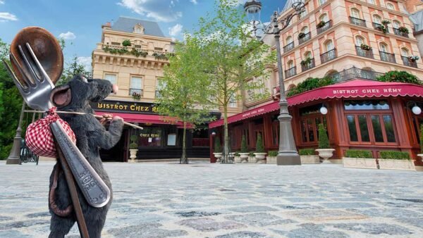 Ratatouille, une souris avec un sac d'ustensiles, debout dans une rue pavée.