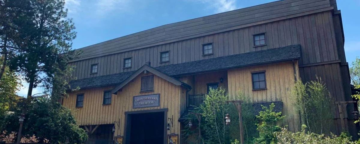 Un grand bâtiment de style grange en bois avec une pancarte indiquant "Théâtre Chaparral" sous un ciel bleu clair, entouré d'arbres verts luxuriants.