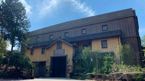 Un grand bâtiment de style grange en bois avec une pancarte indiquant "Théâtre Chaparral" sous un ciel bleu clair, entouré d'arbres verts luxuriants.