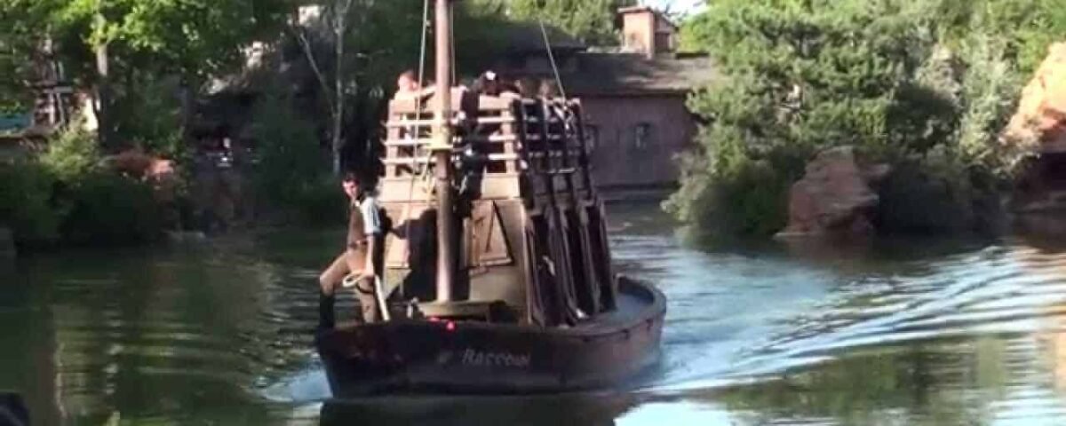 Un petit bateau pirate rustique nommé "River Rogue" avec quelques personnes à bord, naviguant sur des eaux calmes entourées d'une verdure luxuriante.