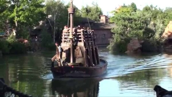 Un petit bateau pirate rustique nommé "River Rogue" avec quelques personnes à bord, naviguant sur des eaux calmes entourées d'une verdure luxuriante.