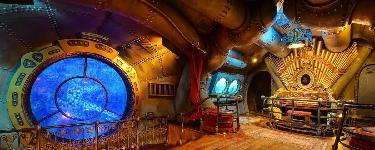 Intérieur d'une pièce sur le thème steampunk inspirée des "Mystères du Nautilus", avec une ferronnerie élaborée, comprenant une grande fenêtre circulaire ressemblant à une fenêtre sous-marine, un éclairage d'ambiance et un mobilier vintage.