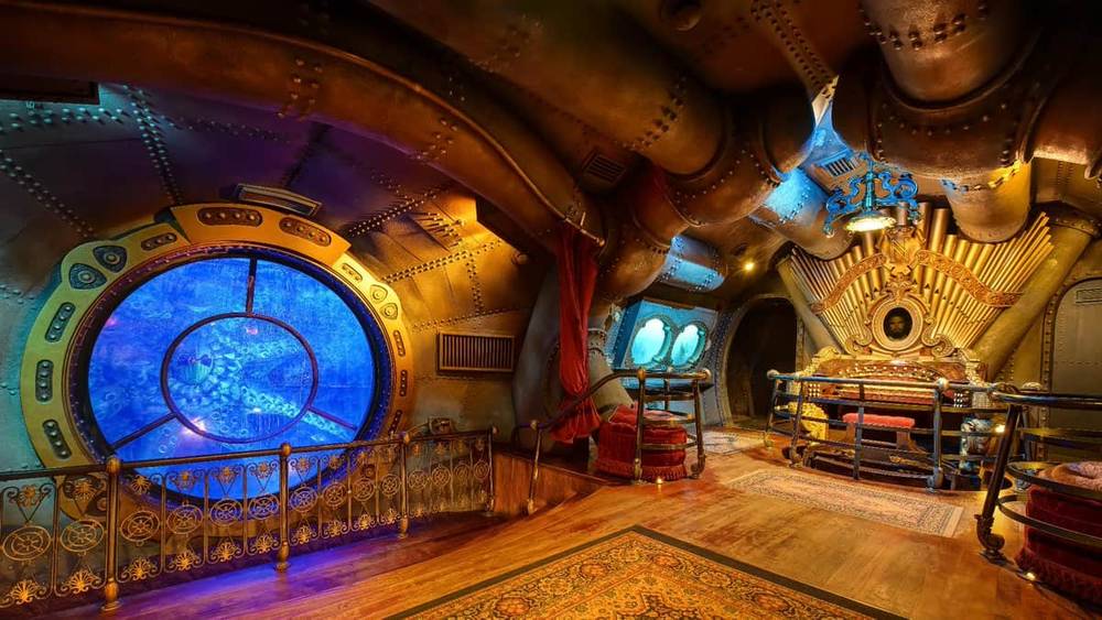 Intérieur d'une pièce sur le thème steampunk inspirée des "Mystères du Nautilus", avec une ferronnerie élaborée, comprenant une grande fenêtre circulaire ressemblant à une fenêtre sous-marine, un éclairage d'ambiance et un mobilier vintage.