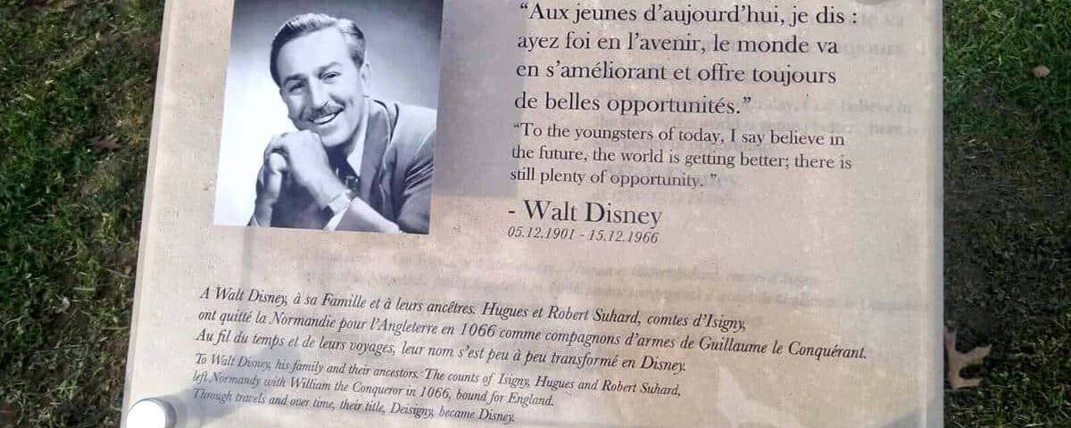 Plaque commémorative sur herbe, représentant une photo de Walt Disney et une citation en français et en anglais sur ses origines, dédicaçant des perspectives positives pour l'avenir, installée dans un parc.