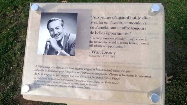 Plaque commémorative sur herbe, représentant une photo de Walt Disney et une citation en français et en anglais sur ses origines, dédicaçant des perspectives positives pour l'avenir, installée dans un parc.