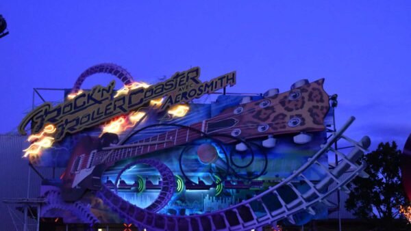 Enseigne lumineuse pour le "Rock'n Roller Coaster avec Aerosmith" comportant une piste de montagnes russes et une guitare au crépuscule.
