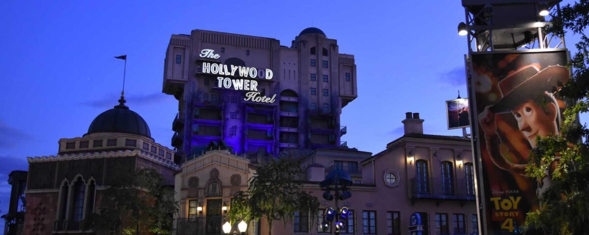 Vue au crépuscule du Hollywood Tower Hotel avec une signalisation violette lumineuse, juxtaposée à une affiche vibrante du film Toy Story 4 mettant en vedette Woody, située dans un parc à thème de Disneyland Paris.