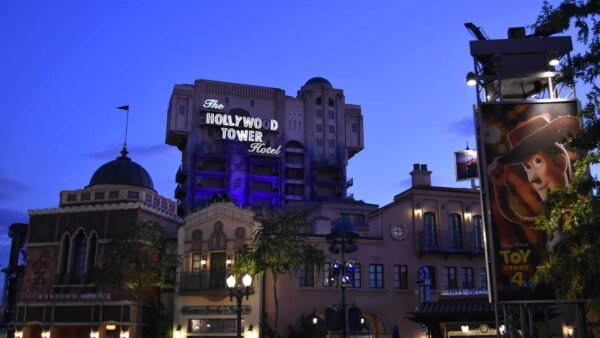 Vue au crépuscule du Hollywood Tower Hotel avec une signalisation violette lumineuse, juxtaposée à une affiche vibrante du film Toy Story 4 mettant en vedette Woody, située dans un parc à thème de Disneyland Paris.
