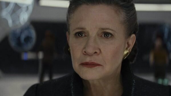 Carrie Fisher dans le rôle de la princesse Leia Organa, l'air inquiète, dans un centre de commandement futuriste avec des accents bleus et des figures floues en arrière-plan.