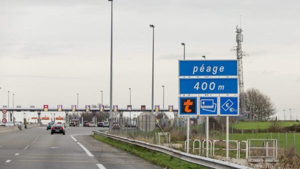 Une autoroute très fréquentée avec un panneau de péage en approche indiquant « péage 400 m » ainsi que des symboles de paiement. Des voitures sont visibles se dirigeant vers les barrières de péage sous un ciel couvert, sur elles
