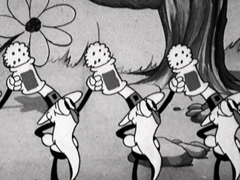 Image animée en noir et blanc tirée de "Silly Symphonies" montrant une file de pissenlits de dessins animés portant des chaussures et des gants, chacun tenant une valise, marchant dans un décor forestier fantaisiste.