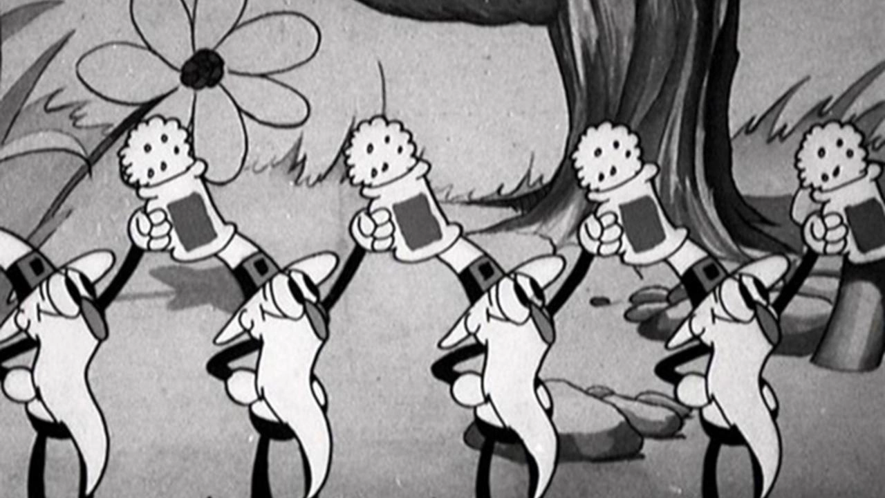 Image animée en noir et blanc tirée de "Silly Symphonies" montrant une file de pissenlits de dessins animés portant des chaussures et des gants, chacun tenant une valise, marchant dans un décor forestier fantaisiste.