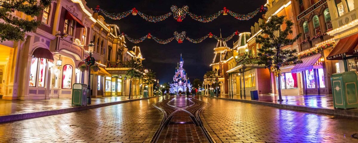 Une vue nocturne animée de la rue principale de Disneyland Paris, ornée de guirlandes lumineuses, menant au loin vers l'emblématique château de Cendrillon.