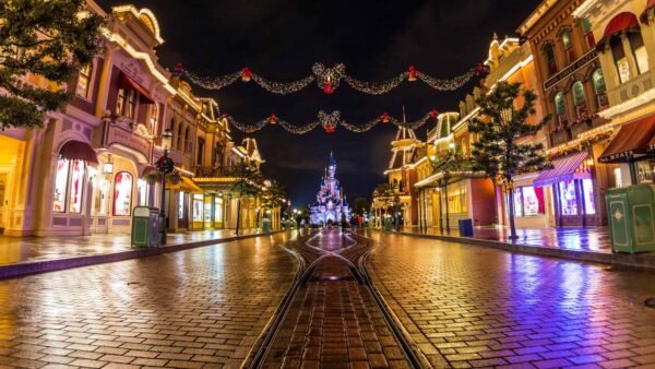 Une vue nocturne animée de la rue principale de Disneyland Paris, ornée de guirlandes lumineuses, menant au loin vers l'emblématique château de Cendrillon.