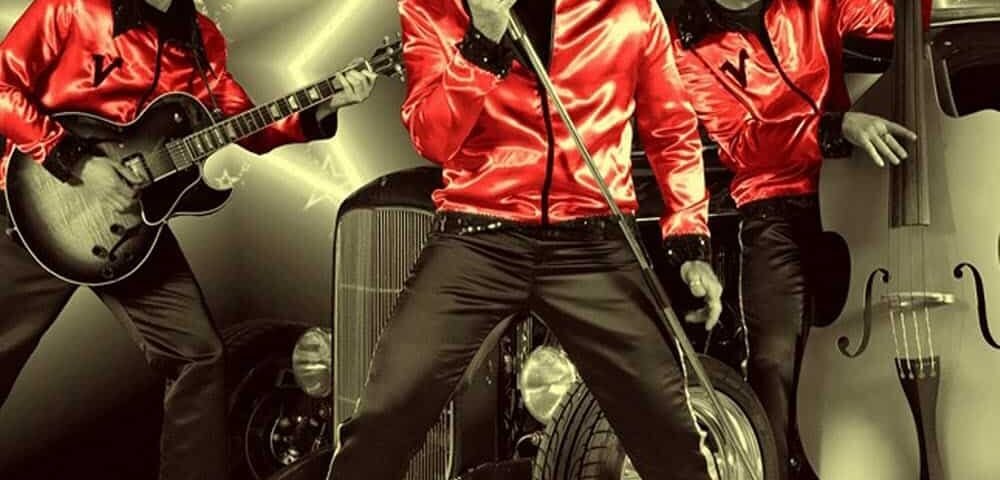 Trois membres d'un groupe vêtus de vestes rouges posant avec des instruments de musique ; un guitariste, un chanteur et un bassiste, avec une voiture de collection et des effets étoilés en fond. Cette séance photo