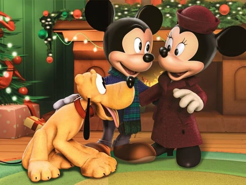 Mickey Mouse et Minnie Mouse dans une salle de fête, se tenant la main avec Pluto le chien à leurs côtés, entourés de décorations et de cadeaux "Il était deux fois Noël".