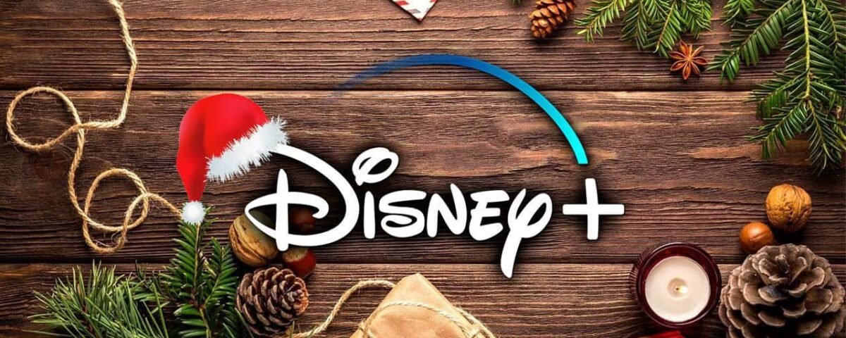 Logo Disney+ avec un chapeau de Père Noël sur fond en bois, entouré de branches de pin, de pommes de terre, d'une bougie, d'un cadeau emballé et de décorations festives de Noël.