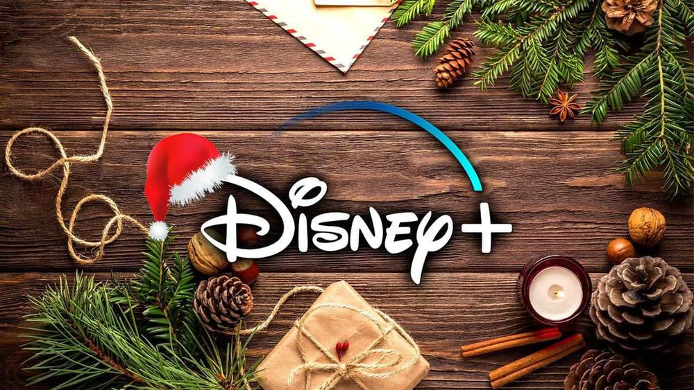 Logo Disney+ avec un chapeau de Père Noël sur fond en bois, entouré de branches de pin, de pommes de terre, d'une bougie, d'un cadeau emballé et de décorations festives de Noël.