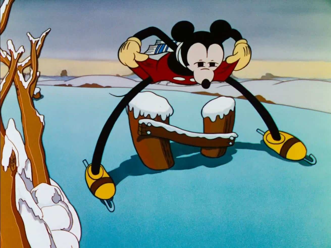 Mickey Mouse patine sur la glace, jambes écartées et bras tendus pour l'équilibre, avec un paysage hivernal en arrière-plan. La neige recouvre une partie du sol et des branches d'arbres.