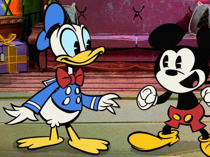 Donald Duck et Mickey Mouse, tous deux personnages animés, se tiennent debout dans une pièce colorée et légèrement échevelée, l'air heureux et gesticulant pendant qu'ils discutent pendant Joyeux Noël.
