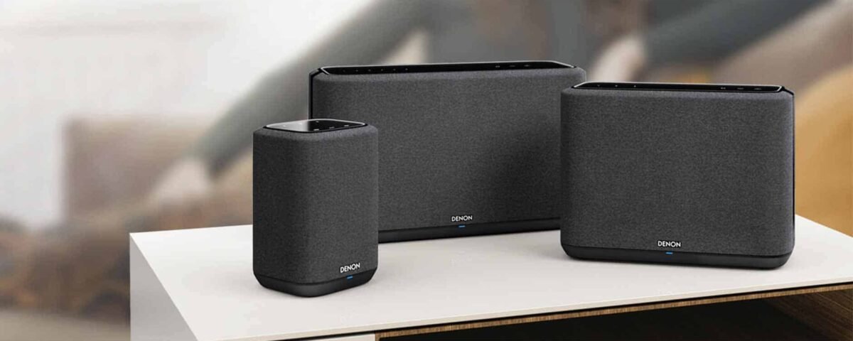 Trois enceintes Wi-Fi Denon modernes recouvertes de tissu noir, exposées sur une table en bois dans une pièce élégamment décorée.