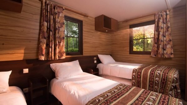 Une cabine confortable en bois au Davy Crockett Ranch avec deux lits simples recouverts de couvertures à motifs, une table de chevet, des rideaux aux fenêtres et une vue sur la verdure à l'extérieur.