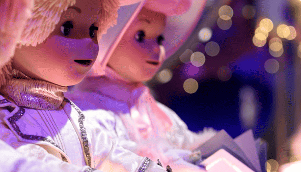 Deux ours en peluche vêtus de costumes blancs et argentés, ornés de chapeaux sur le thème de la chanson, représentés dans un décor festif avec un éclairage tamisé et des lumières de Noël floues en arrière-plan.