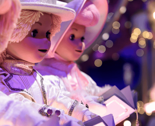 Deux ours en peluche vêtus de costumes blancs et argentés, ornés de chapeaux sur le thème de la chanson, représentés dans un décor festif avec un éclairage tamisé et des lumières de Noël floues en arrière-plan.