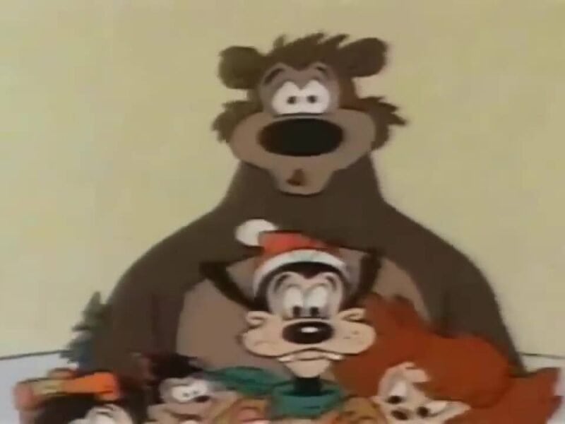 Un groupe d'animaux de dessins animés, dont un gros ours, un ours plus petit portant un chapeau et trois créatures colorées, se blottissant les unes contre les autres avec des expressions surprises pendant Noël.