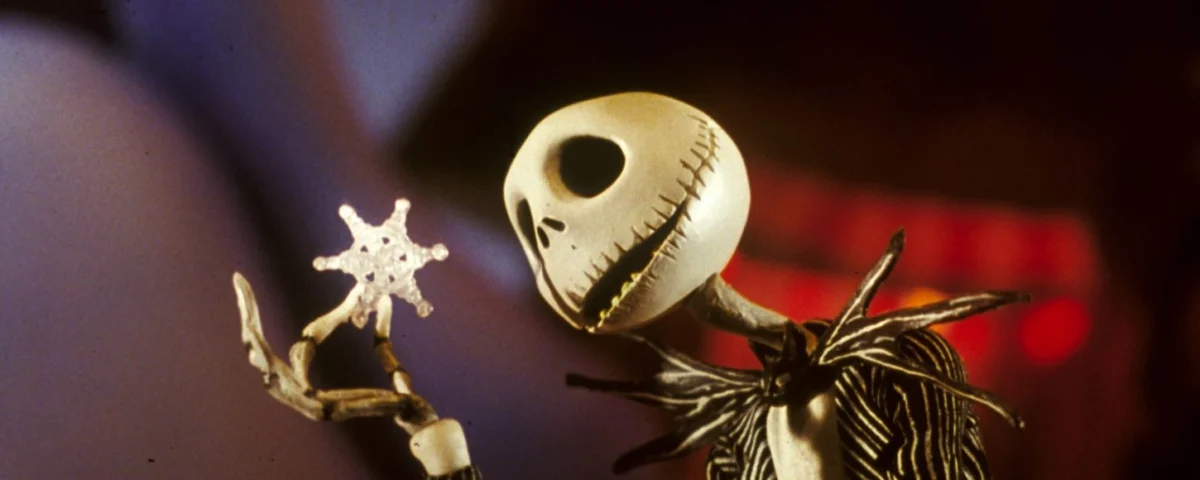 Monsieur Jack de "L'Étrange Noël de Monsieur Jack", créé par Burton, tenant un petit flocon de neige scintillant, avec un arrière-plan chaud et flou soulignant sa curieuse expression.